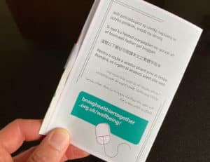 A hand holding a copy of a leaflet with wellbeing information, the page shows information in different languages