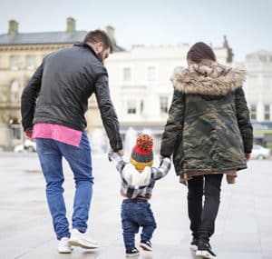Man and woman walking down the street with a young child between them, holding the child's hands.