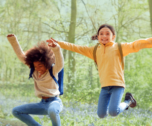 Two children smiling and jumping in a forest.