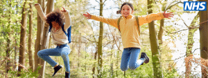 Dy fëmijë duke buzëqeshur dhe duke kërcyer në një pyll.