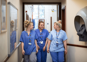 3 healthcare professionals walking down a hallway, smiling.