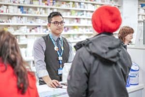 Pharmacist stood at a counter, serving a customer